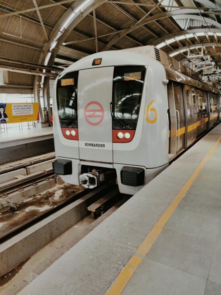 A sleek metro train arrives at a modern New Delhi railway station platform.