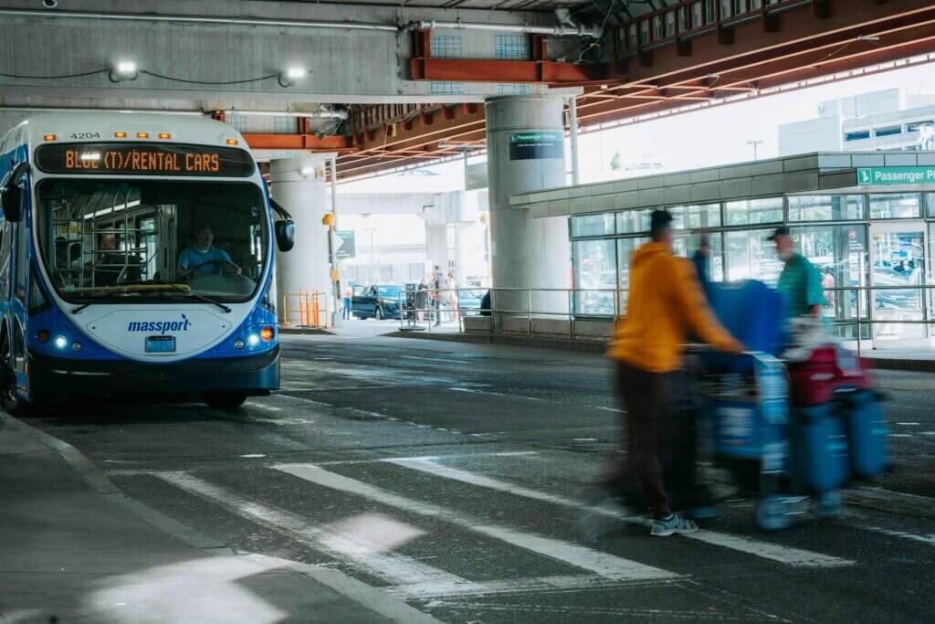 Busy airport scene showing travelers in motion and a rental car bus waiting under a covered terminal. PH Bus Terminals, Routes & Schedules