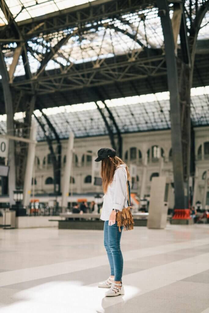 Young woman waiting at a modern railway station in urban setting, showcasing travel and commuting themes.