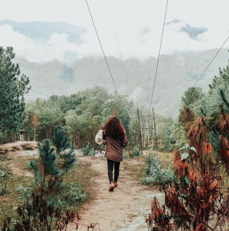A person walking on a dirt path in Sagada, surrounded by lush greenery and distant mountains.