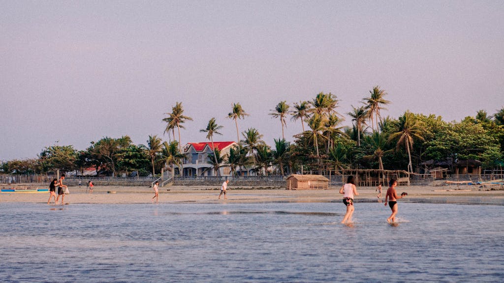 Beachgoers enjoy a tranquil walk along a tropical shore with palm trees and clear skies. Manila_to_Siargao