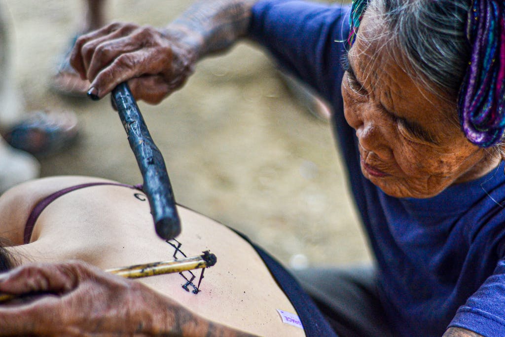 Elderly woman performing traditional hand-tap tattooing on a younger person's back in Buscalan  Kalinga, Philippines.