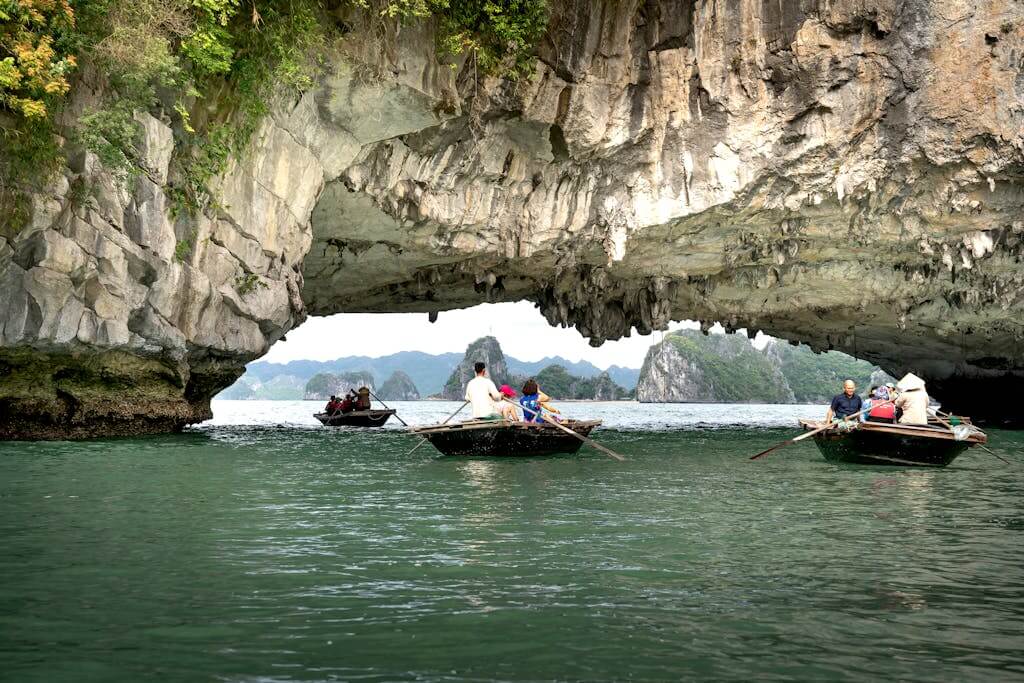 Explore  a  Vietnam trip to breathtaking limestone arch with boats on a serene waterway, surrounded by nature.