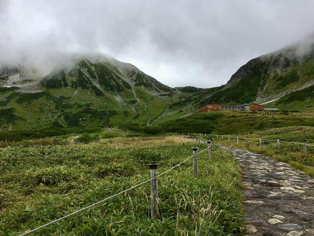 Explore the lush greenery and mountain huts of Tateyama, Japan, with a misty mountain backdrop. Japanese Alps tour
