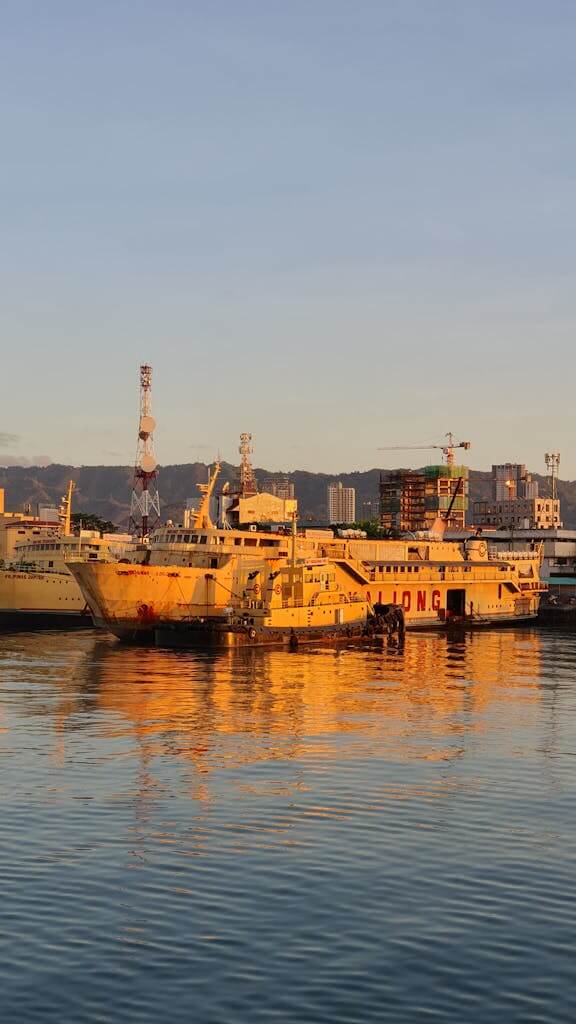 Ships docked at a harbor during a vibrant golden sunset, reflecting on the calm water. Sampaloc to Batangas pier commute