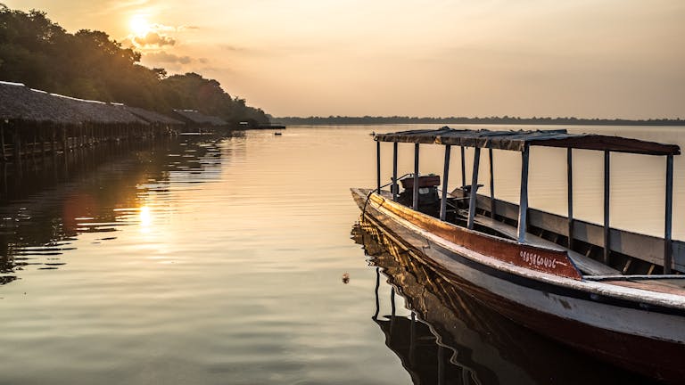 Tranquil scene of a wooden boat on a lake at sunset in Siem Reap Cambodia tour