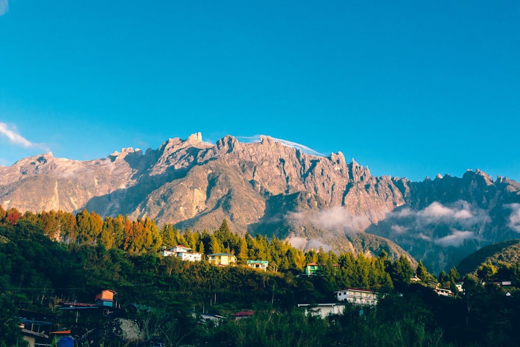 A breathtaking aerial view of Mount Kinabalu with vibrant blue skies and a charming village below.