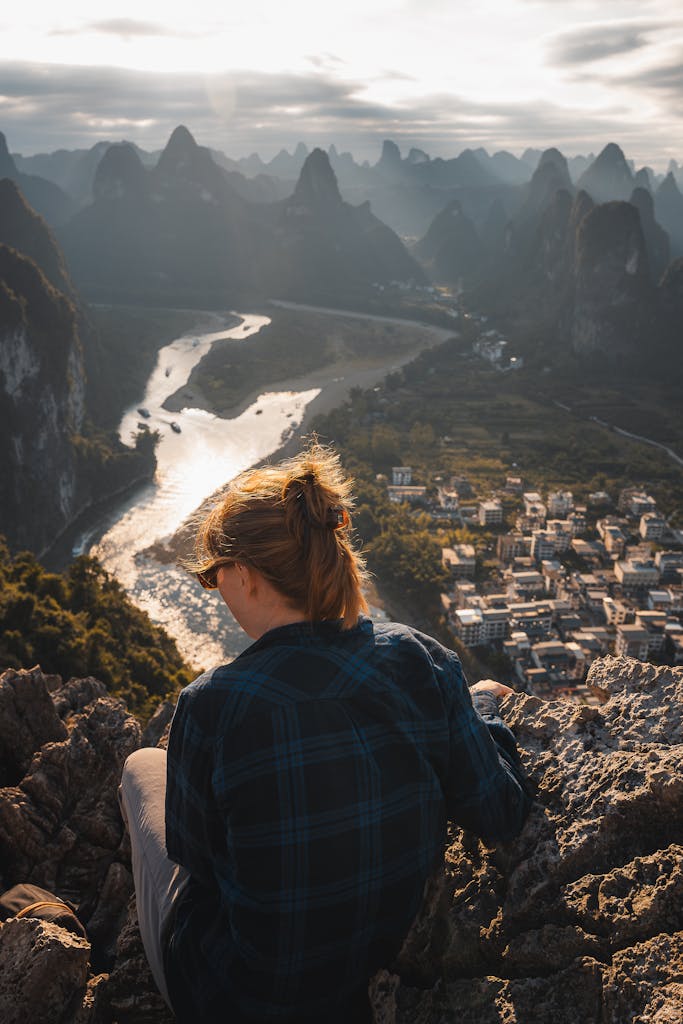 A person overlooking the picturesque Guilin landscape with flowing river and karst peaks at sunset.