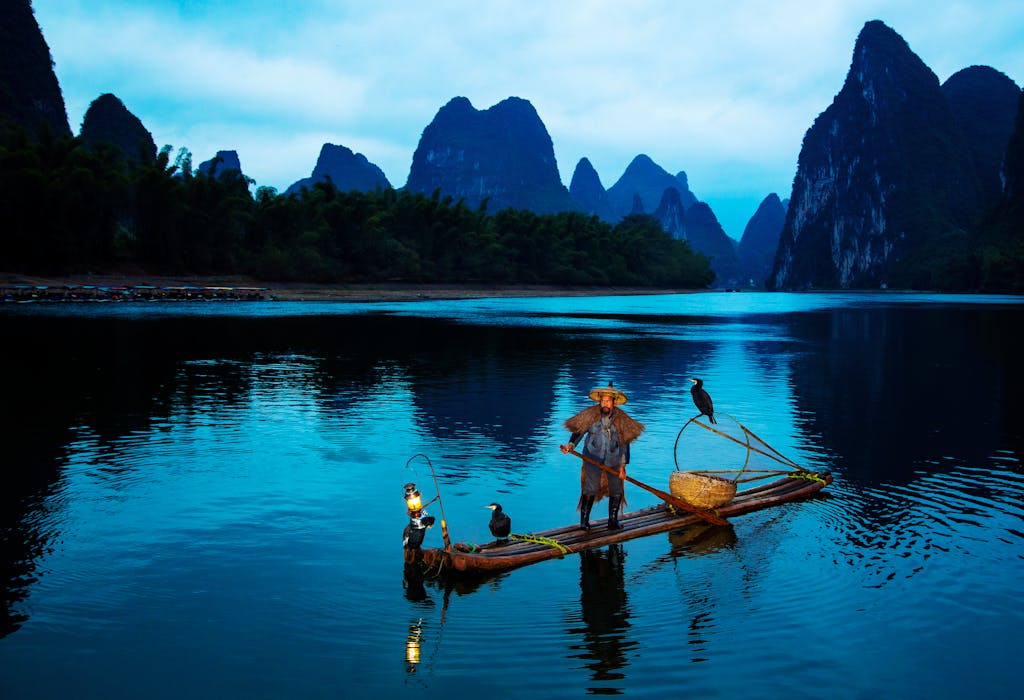 A serene scene of a cormorant fisherman at dusk on the Li River in Guangxi, China.