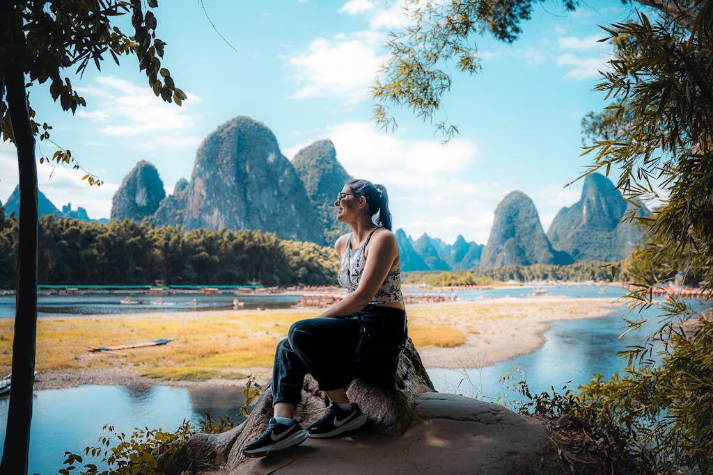 A woman sitting on a rock, admiring the stunning karst landscape of Guilin, China.