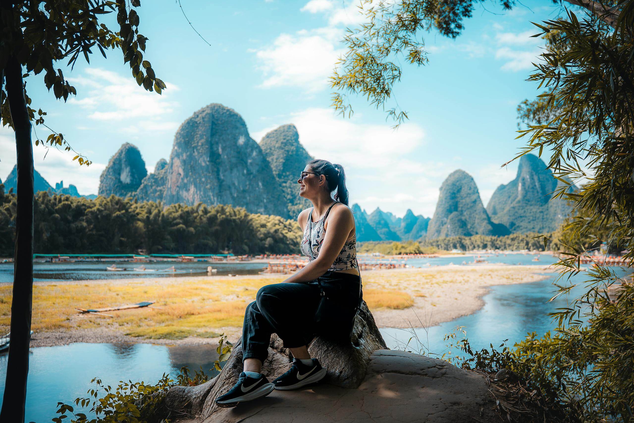 A woman sitting on a rock, admiring the stunning karst landscape of Guilin, China.