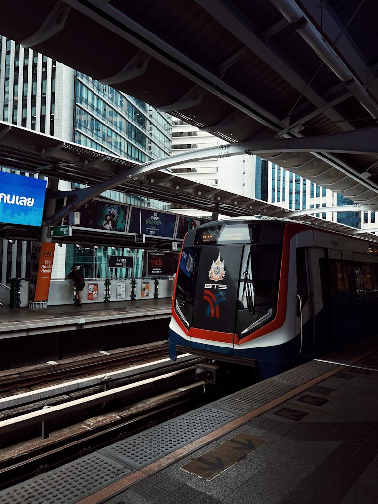 BTS Skytrain arrives at Bangkok station amidst urban high-rise buildings. Bangkok Thailand commute
