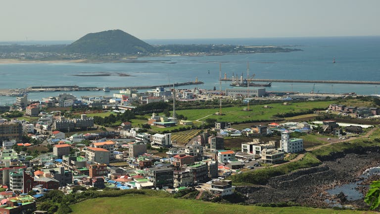 Discover the vibrant coastal cityscape of Jeju Island, featuring lush greenery and modern architecture by the sea.