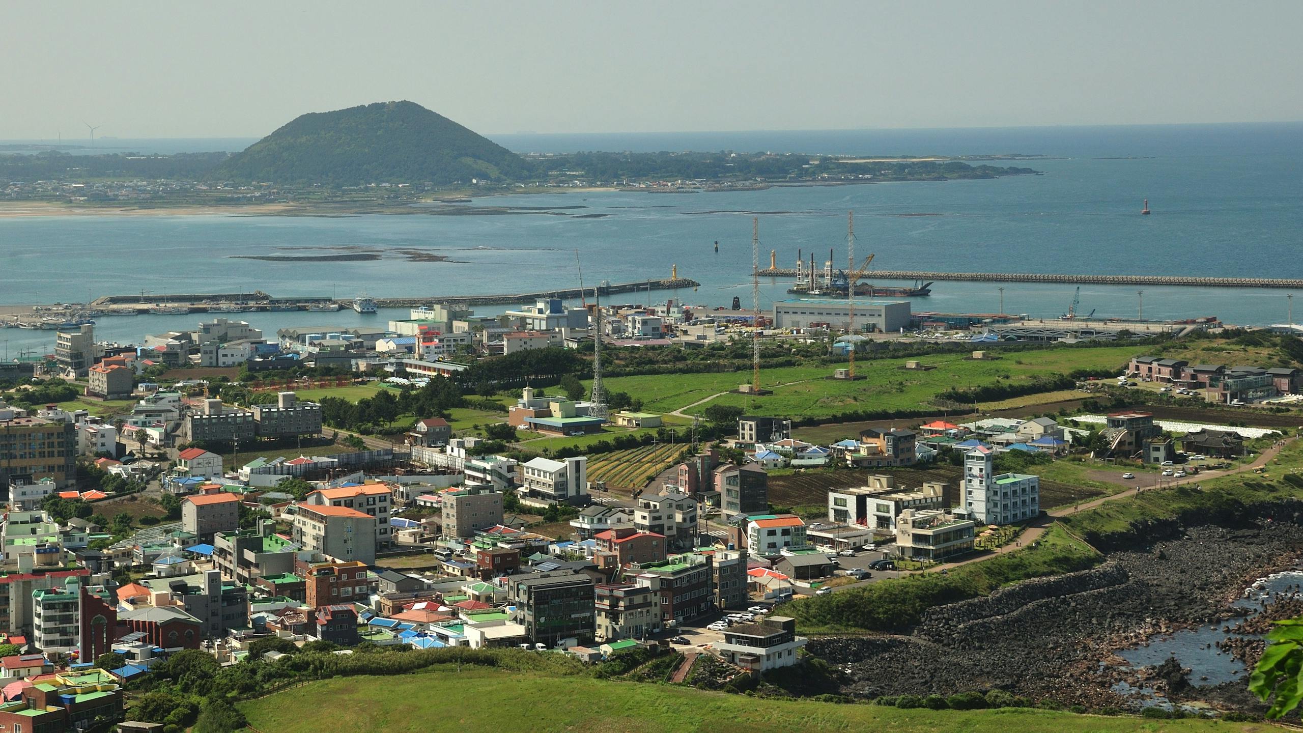Discover the vibrant coastal cityscape of Jeju Island, featuring lush greenery and modern architecture by the sea.