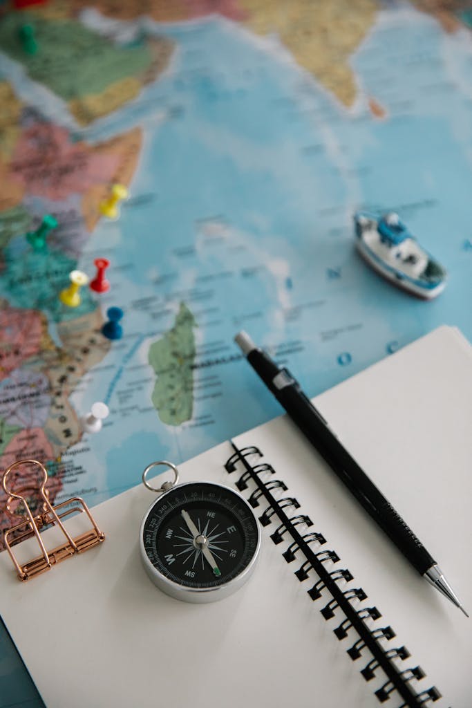 Flat lay of travel essentials including a navigational compass, pencil, notepad, and map for trip planning. MappedAtlas movement system guide