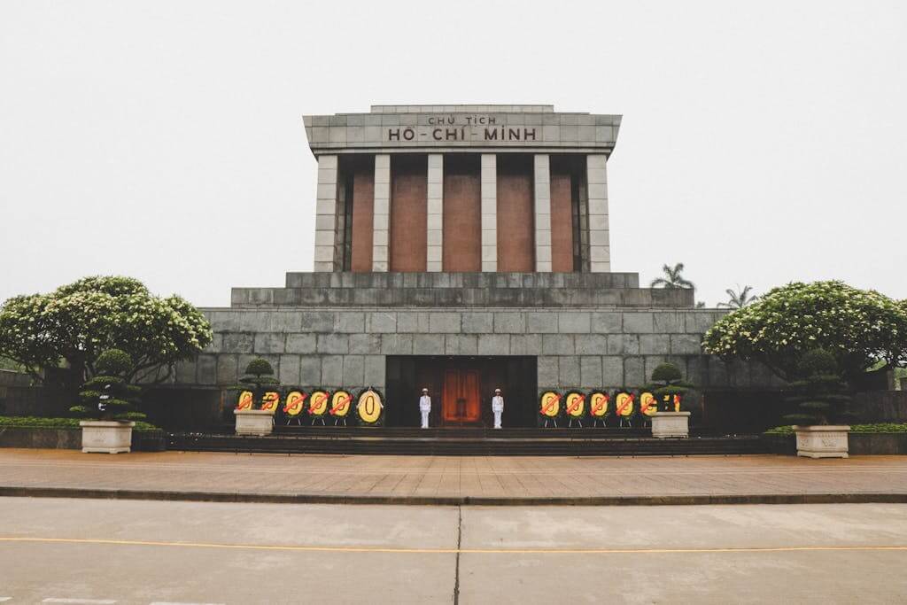 Front view of the iconic Ho Chi Minh Mausoleum in Hanoi, Vietnam with guards and floral wreaths.