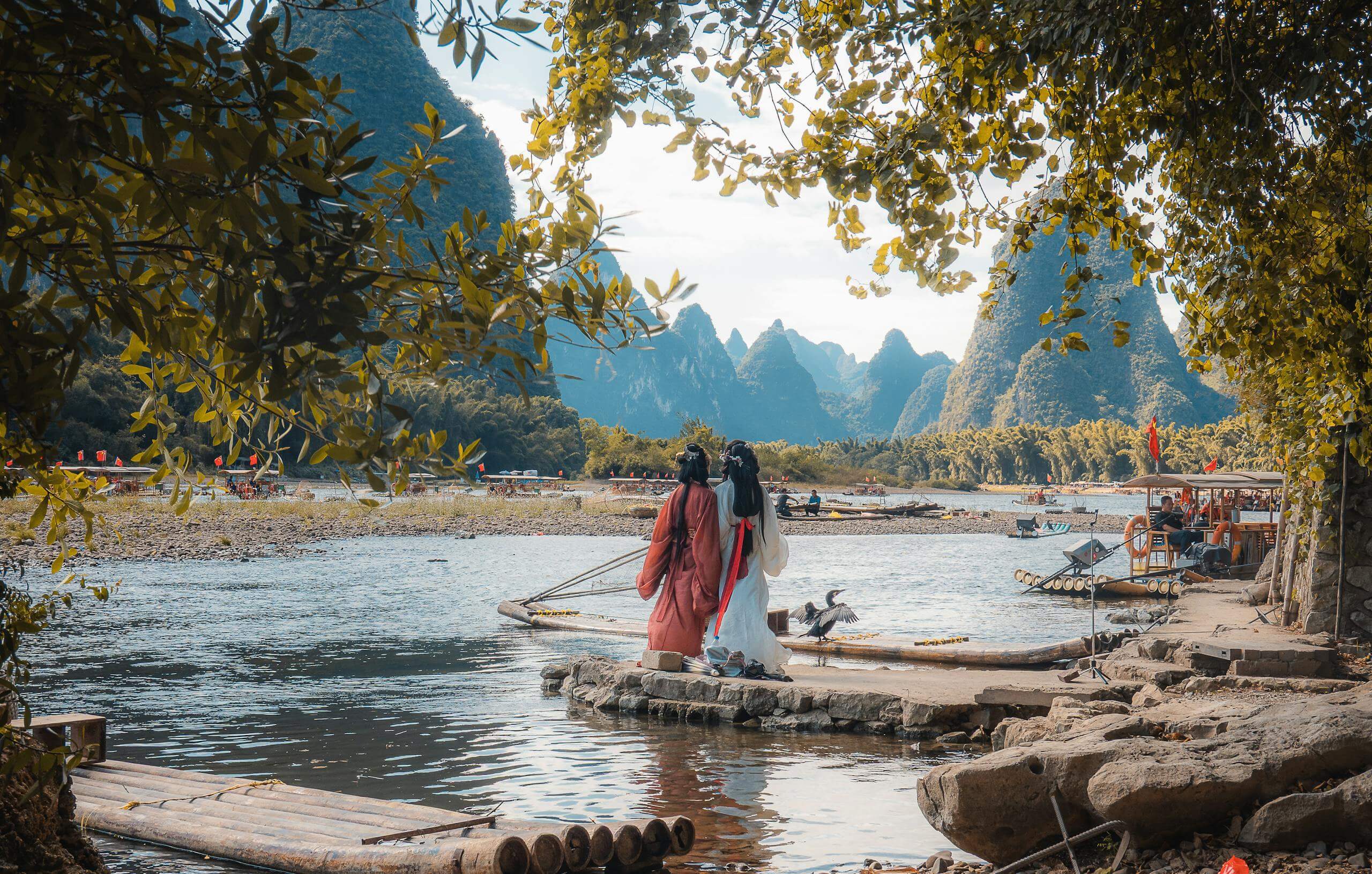 People in traditional attire by the scenic Li River and karst mountains in Guilin, China.