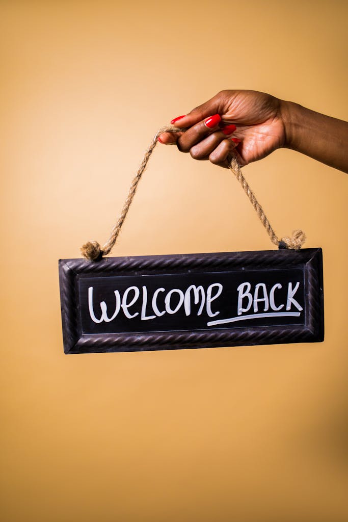 Person holding a welcome back sign against a yellow background, offering inviting vibes.