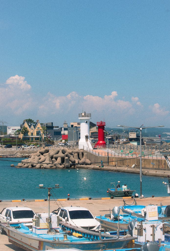 Scenic view of Busan harbor featuring red and white lighthouses, boats, and a coastal town. Busan South Korea Tour