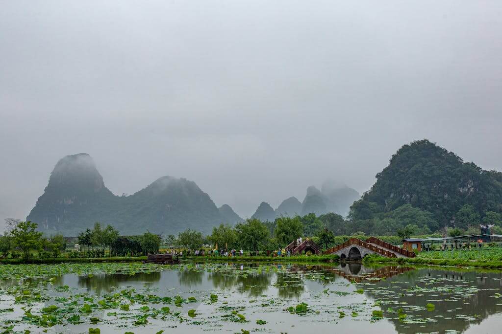 Scenic view of foggy karst mountains reflected in a calm lake with lush greenery. Guilin Yangshuo China tour