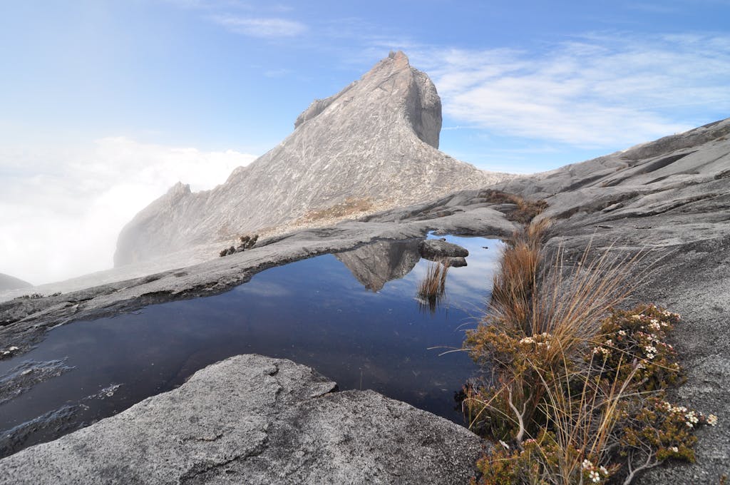 Stunning landscape of Mount Kinabalu in Sabah, Malaysia, with a reflective puddle and clear blue skies. Sabah Malaysia tour
