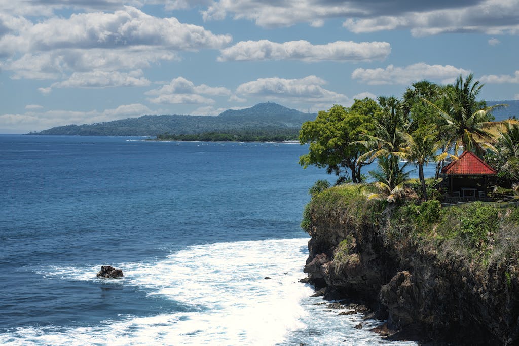 Stunning ocean view from a lush cliffside in Bali, featuring palm trees and vibrant blue waters.
