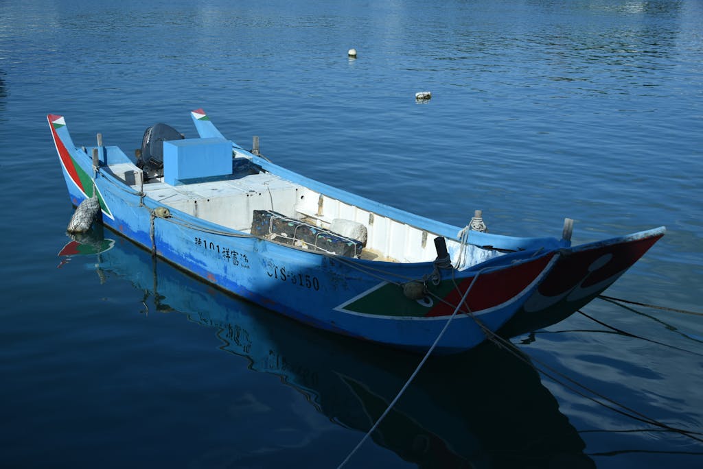 Vibrant blue fishing boat anchored on calm waters, reflecting a peaceful scene.