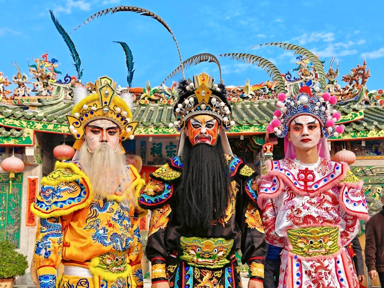 Vibrant display of traditional Chinese opera costumes and makeup against ornate temple backdrop.